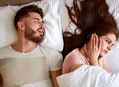 woman covering ears and man snoring