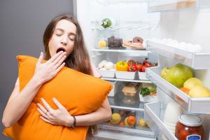 woman yawning and holding a pillow at the fridge